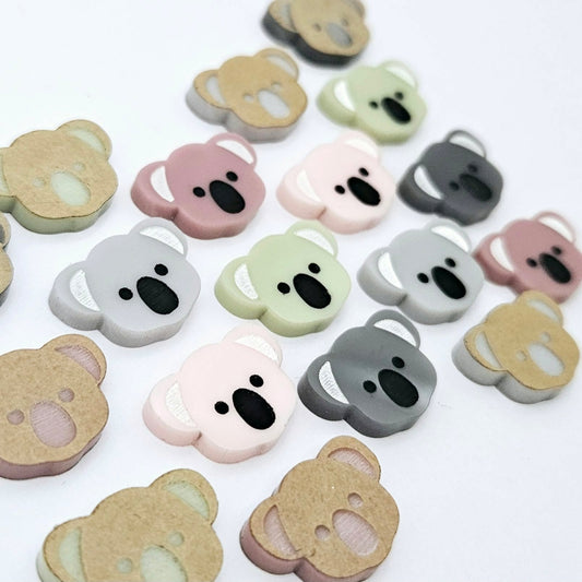 18mm solid acrylic koala stud earring blanks in Grey, Strawberry Milkshake, Dark Grey, Eucalyptus Earth and Dusty Rose, with five paint-filled pairs laid flat and additional unpainted koalas scattered around.