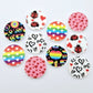 20mm UV printed Love Is Love acrylic stud earring blanks in five colourful designs: Neon Pride, Rainbow Love, Pink & Red Hearts, Black & Red Hearts and Ladybug Love, with all five pairs laid flat together.