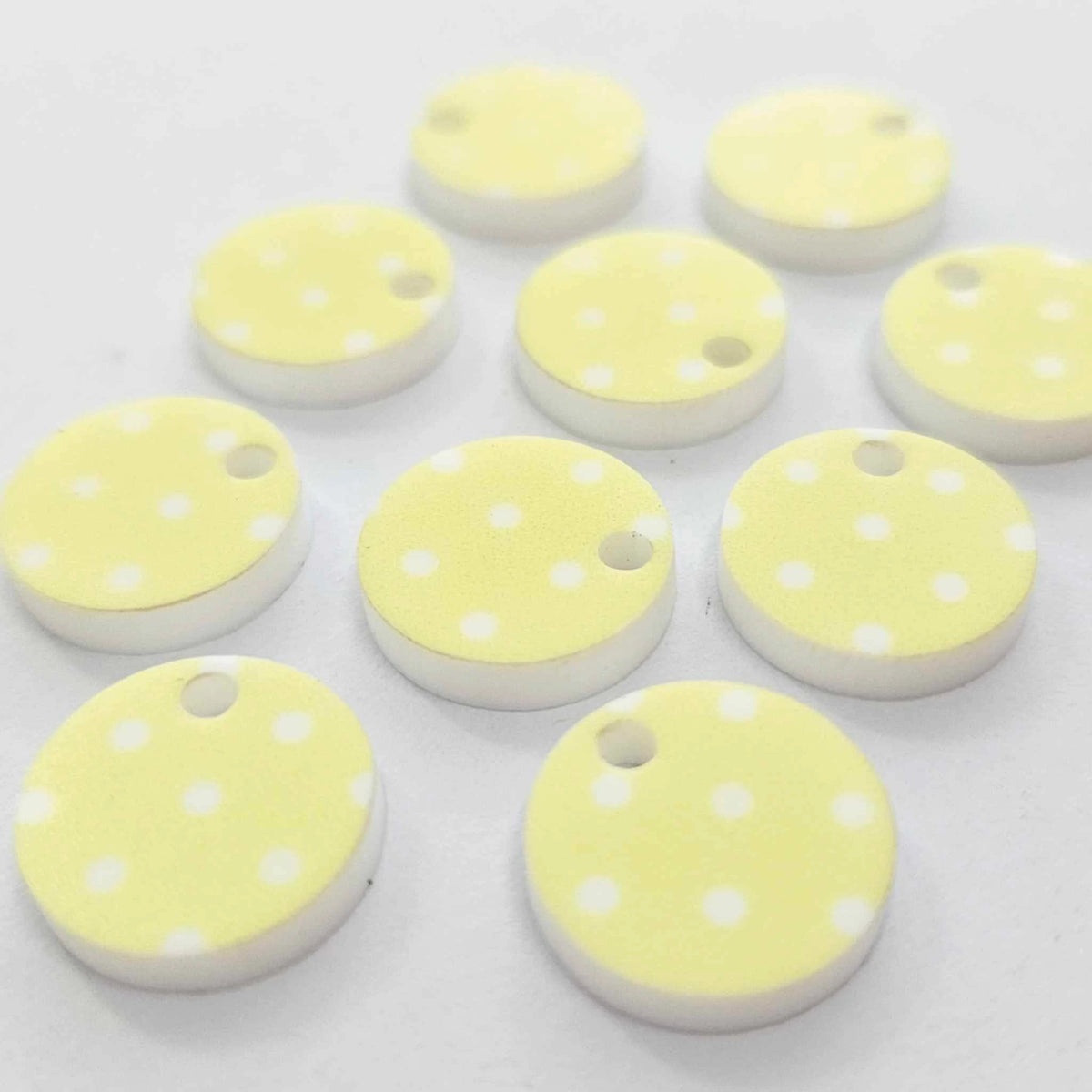 Ten 14mm Pastel Polka Dot UV printed acrylic earring toppers in yellow with white polka dots laying flat